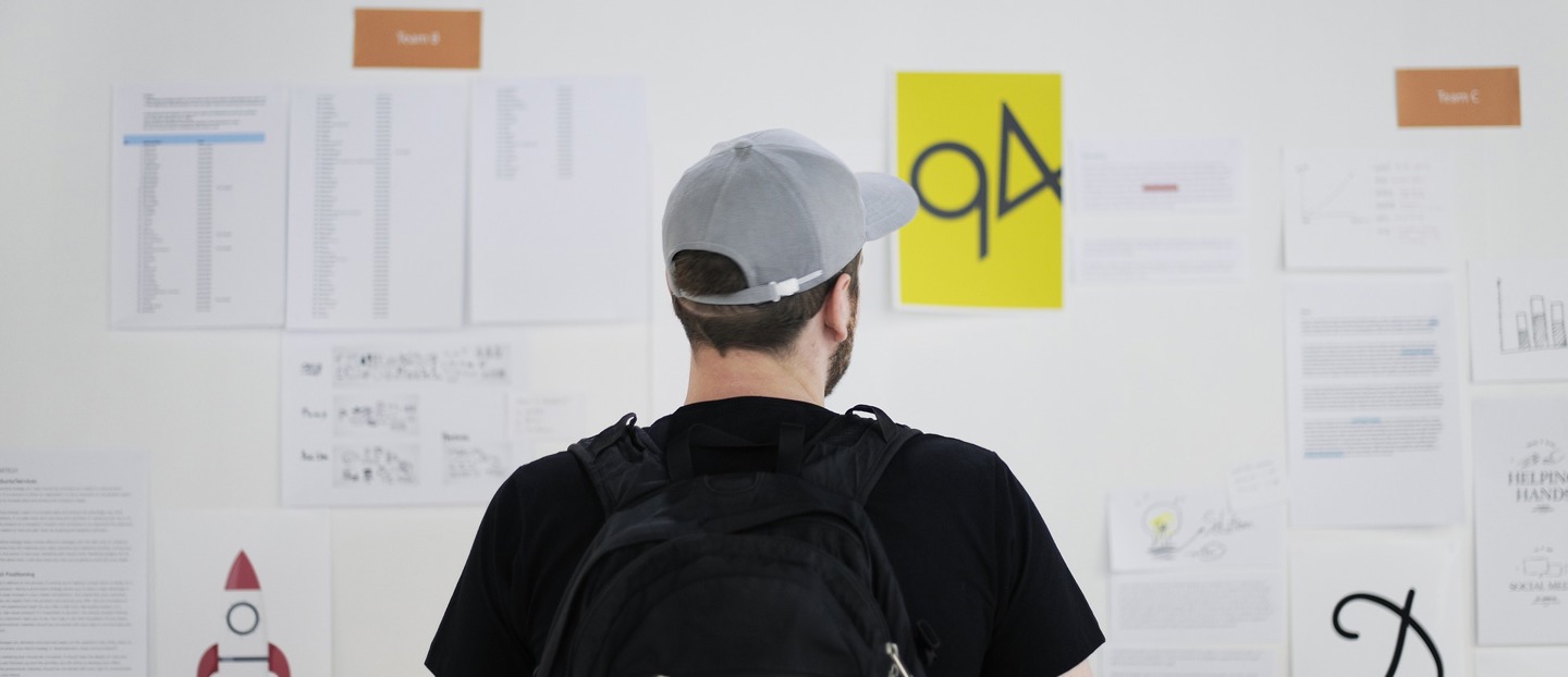 Une homme avec une casquette devant un tableau blanc rempli de feuilles